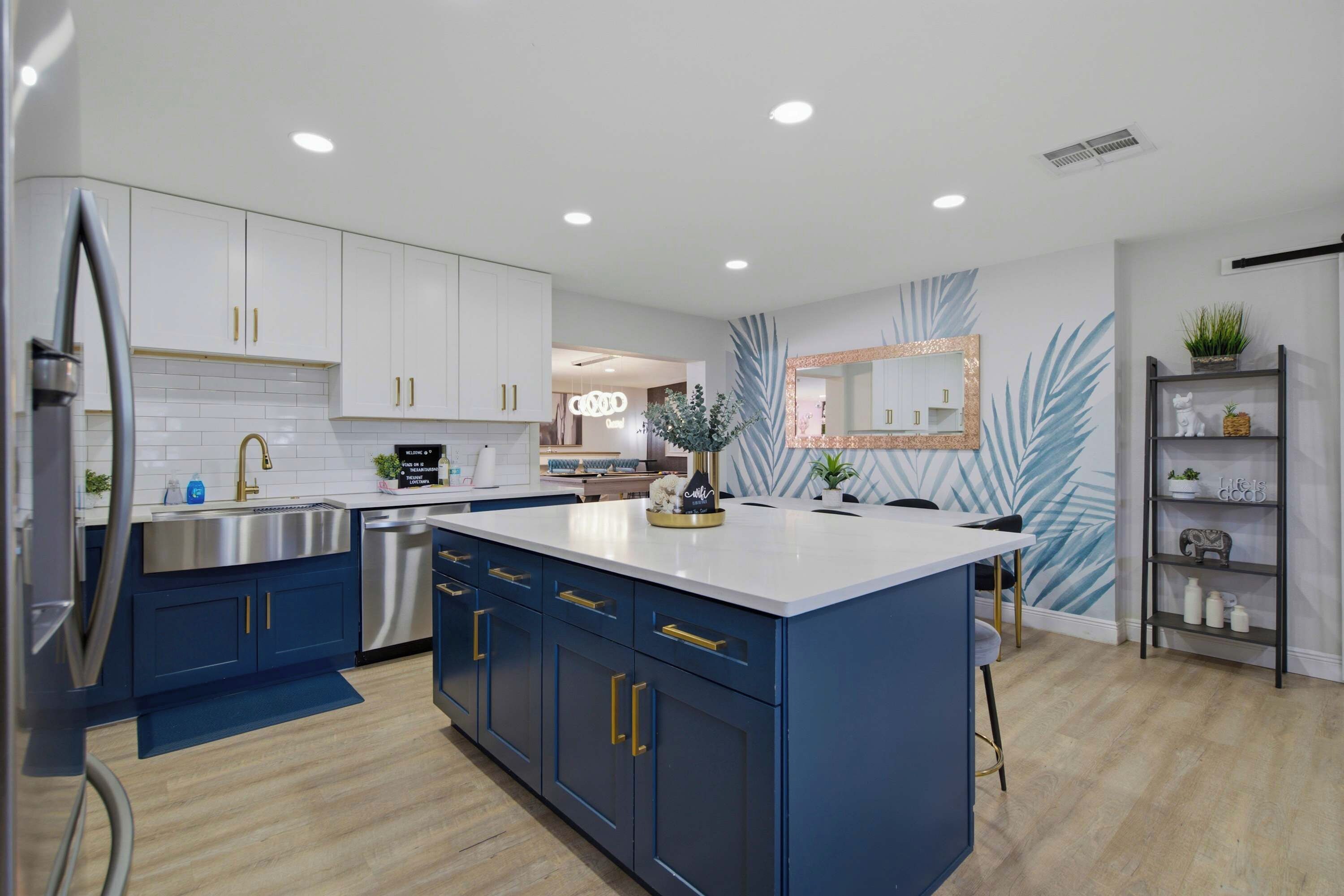 A modern kitchen with white cabinets, a blue island, stainless steel appliances, and a decorative mirror.