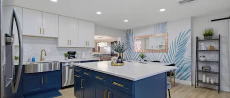 Une cuisine moderne avec des meubles blancs, un îlot central bleu, des appareils en acier inoxydable et un miroir décoratif.