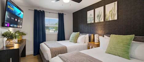 Habitación de hotel con dos camas, un televisor de pantalla plana, un ventilador de techo y obras de arte en la pared.