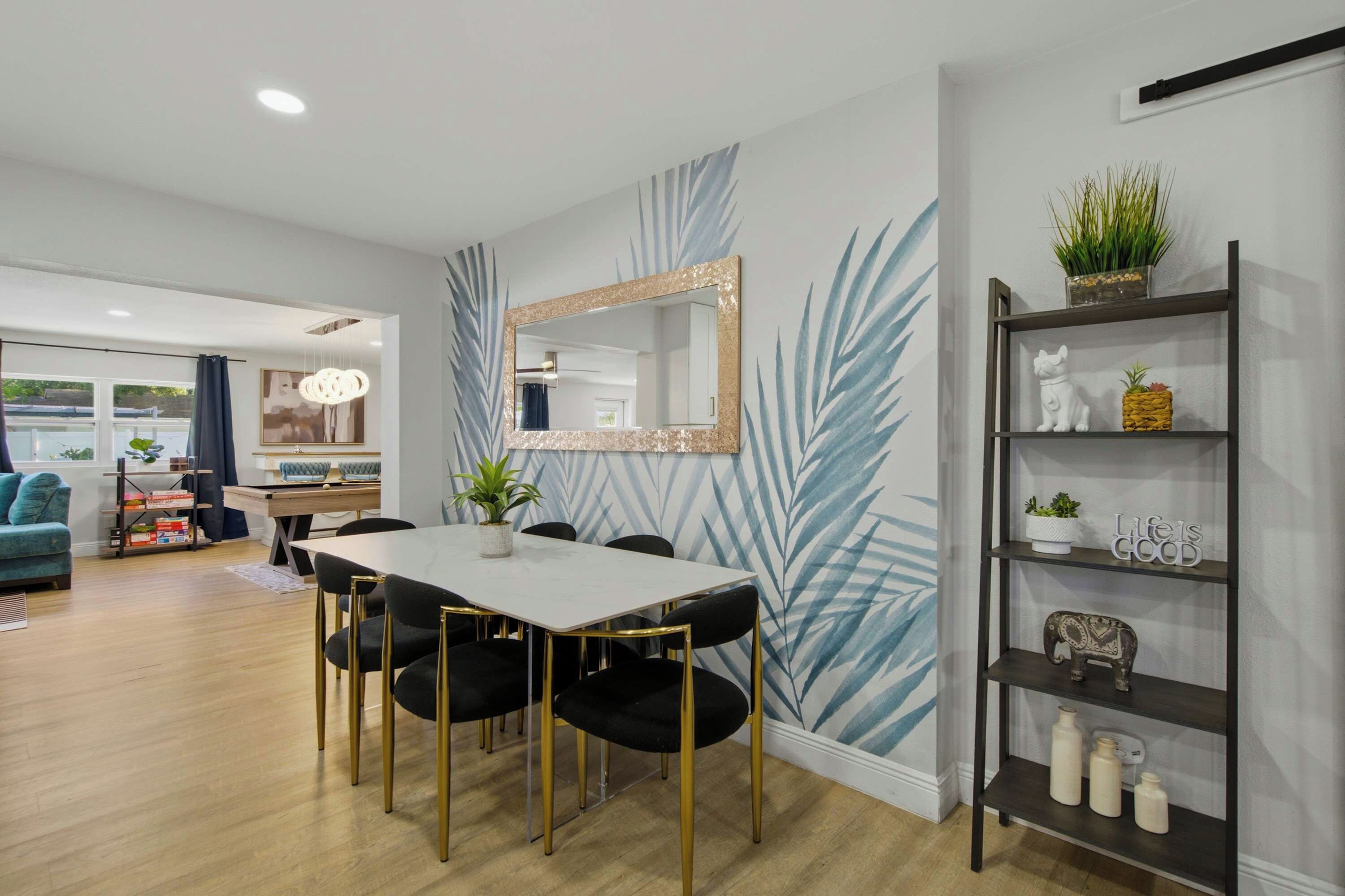 Un espace repas moderne avec une table blanche, des chaises noires et un miroir décoratif.