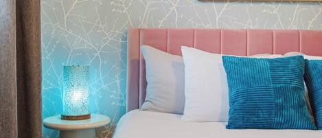 Quarto com cama, travesseiros, mesa de cabeceira, abajur e parede com padrão de galho de árvore.