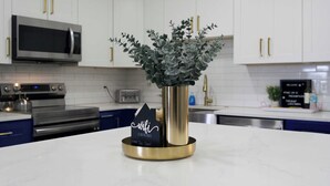A kitchen with white cabinets, a stainless steel microwave, a toaster, and a decorative plant in a gold vase.
