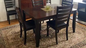 Un comedor con una mesa de madera, seis sillas, un aparador con puerta de cristal y una araña.