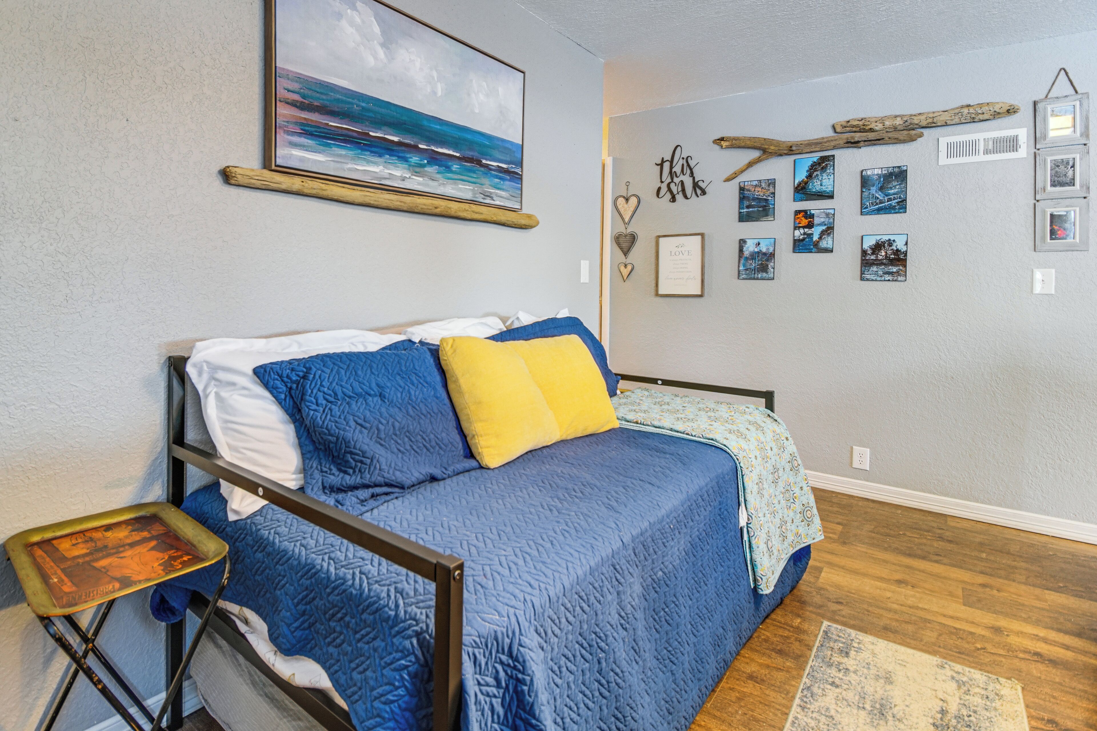 A bedroom with a bed, a small table, a painting, and wall decorations.