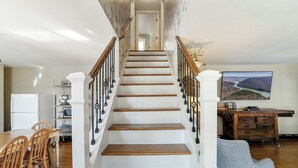 Un escalier avec des marches en bois et des balustrades noires, menant à un palier où se trouvent un coin repas et un téléviseur.