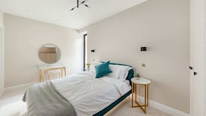 Een slaapkamer met een bed, nachtkastje, ronde spiegel en een klein rond tafeltje met een plant.