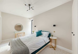 A bedroom with a bed, bedside table, round mirror, and a small round table with a plant. - Luxury New Build 2-Bed, 2-Bath in Wimbledon (London)