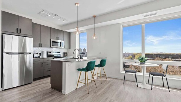 A modern kitchen with a central island, stainless steel appliances, and a large window offering a city view. - 1BR Retreat in Uptown |Walkable | Gym (Minneapolis)