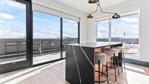 A modern kitchen with a marble countertop, bar stools, and large windows offering a city view. - 1BR Retreat in Uptown |Walkable | Gym (Minneapolis)