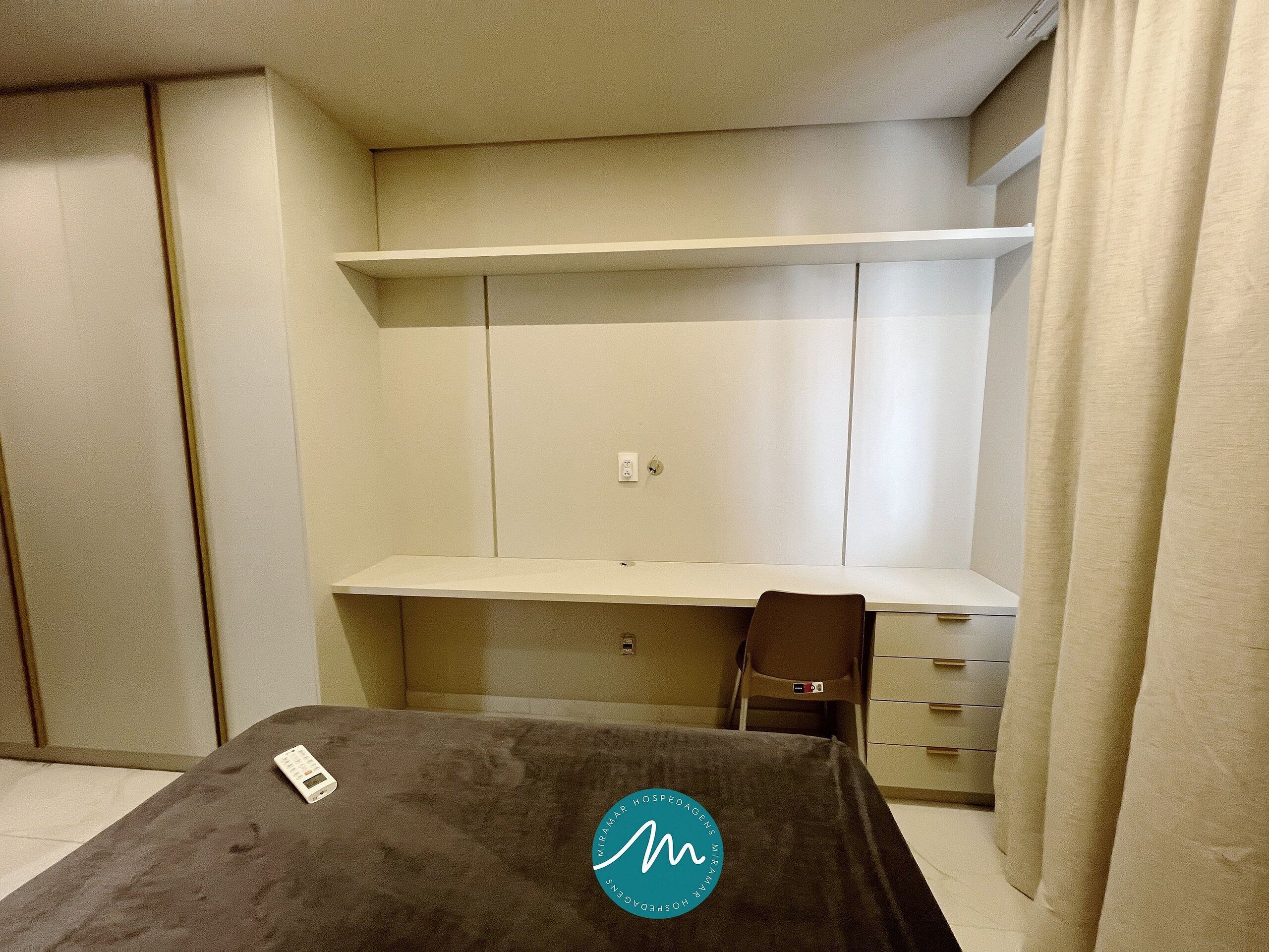 Une chambre à coucher avec un lit, un bureau et une chaise. On y trouve une armoire avec un miroir et une étagère au-dessus du bureau.