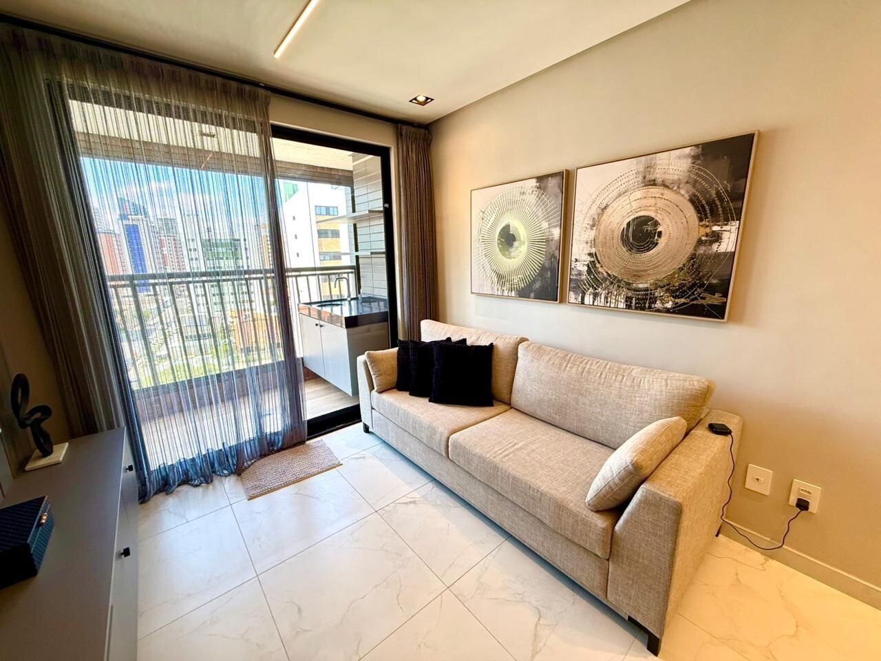 A living room with a sofa, a dining table, a large window with curtains, and artwork on the wall.