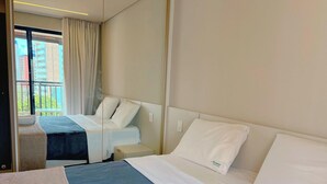 Quarto de hotel com cama, mesa de cabeceira, espelho e janela com cortinas.