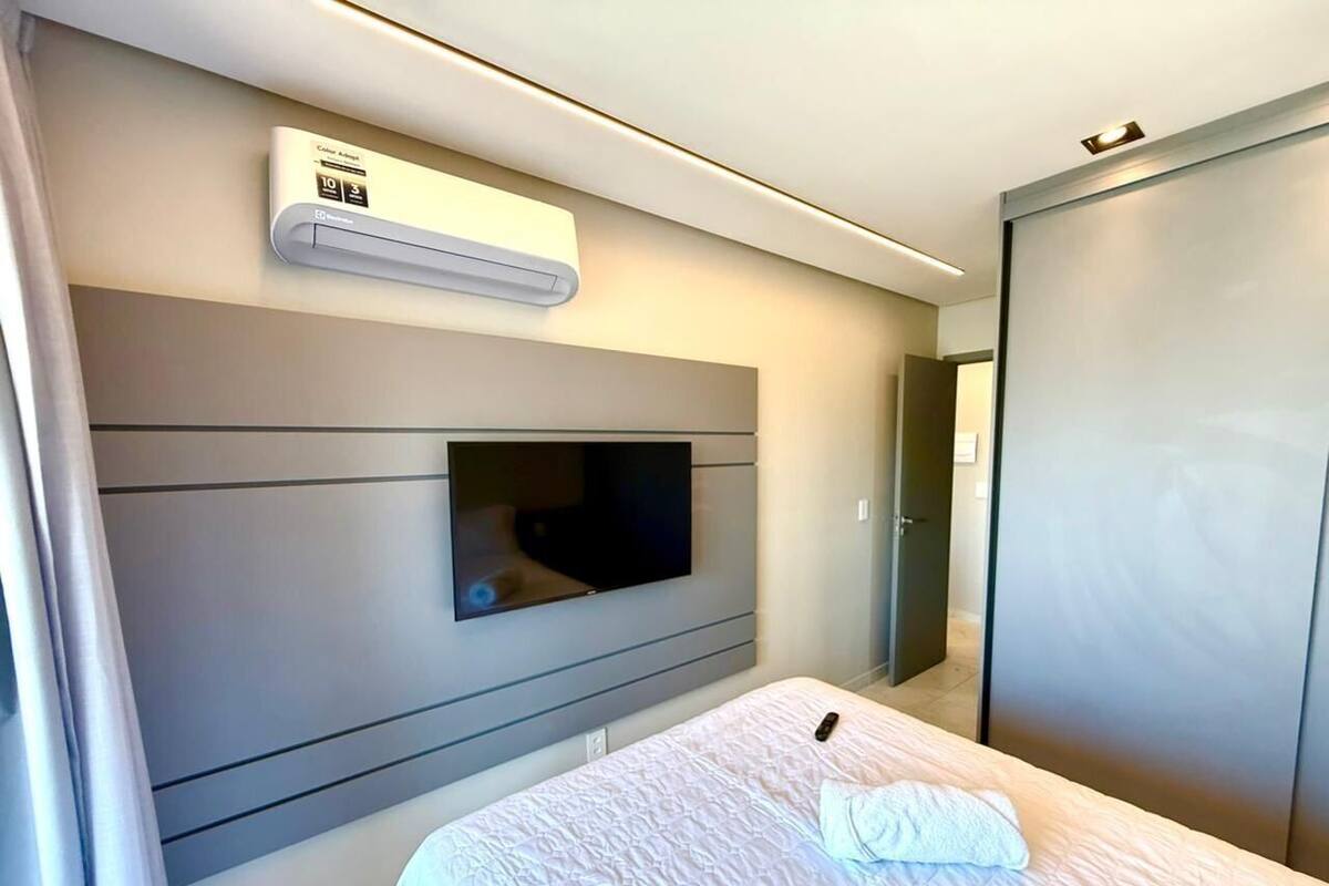 A hotel room with a bed, a television mounted on the wall, and an air conditioning unit above the bed.