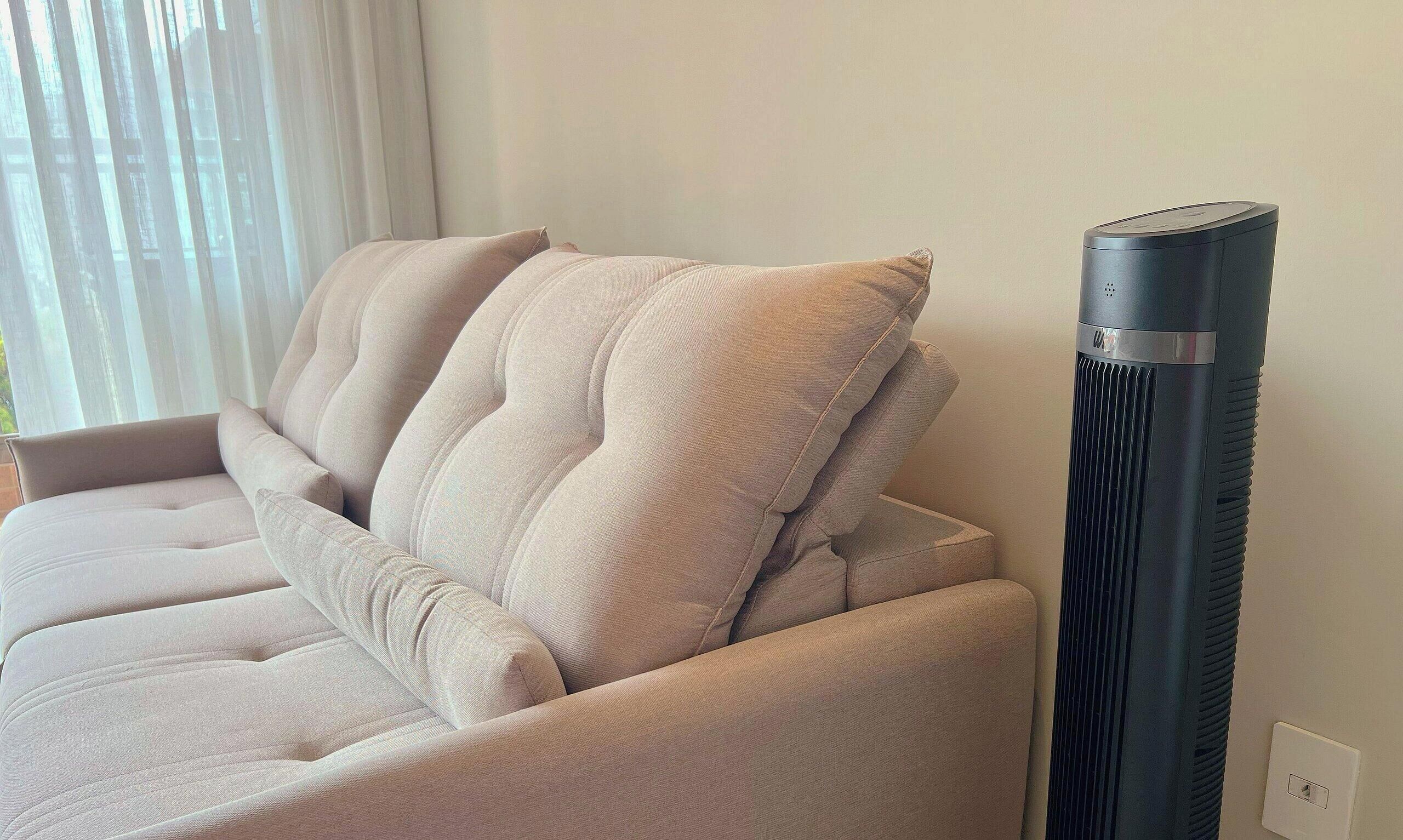 A beige sofa with a tall, cylindrical air purifier next to it.