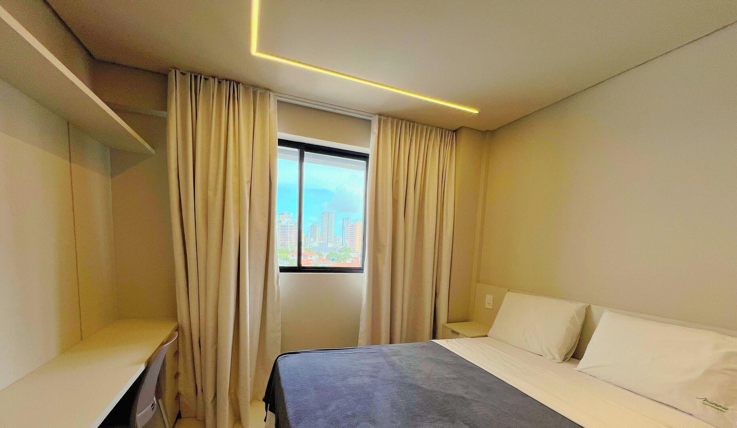 Una camera d'albergo con un letto, una finestra con tende e un comodino, e vista sulla città.