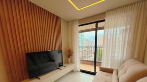 Uma sala de estar moderna com televisão de tela plana, um sofá e varanda com vista para a cidade.