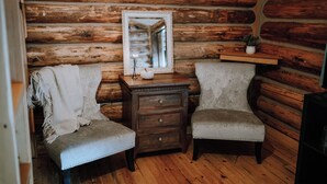 Une chambre rustique aménagée dans un chalet en rondins, avec deux fauteuils rembourrés, une table de chevet en bois et un miroir.