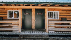 Une cabane en rondins dotée de deux portes portant les inscriptions « Pin » et « Bouleau », de bancs en bois et d’un toit en métal.
