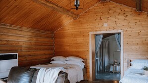 A cozy cabin room with a wooden ceiling, a bed with white bedding, a leather sofa, and a small table with a lamp. - Aspen Cabin: Relaxing Mountain Escape | Sleeps 4 (Clearwater County)