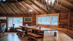 A rustic wooden cabin with a large dining table, benches, and a chandelier. - Aspen Cabin: Relaxing Mountain Escape | Sleeps 4 (Clearwater County)