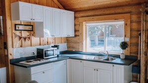 A kitchen with white cabinets, a microwave, a sink, and a window with a view of the outside.
