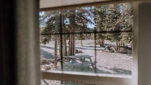 A view through a window of a forested area with a picnic table and rocks.