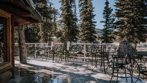 A wooden deck with outdoor seating, surrounded by tall trees and a clear view of the mountains.