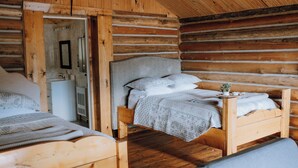 Un dormitorio de cabaña de madera con dos camas, un cabecero de madera y una mesita de noche pequeña con una planta.