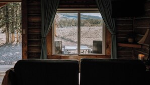 Interior de una cabaña con un ventanal grande que da a un área boscosa.