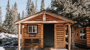 Pieni puinen mökki, jonka edessä on kyltti, jossa lukee: ”Dogwood Shanty”. Siinä on etuovi, ikkuna ja kaksi tuolia ulkona.