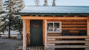 Une cabane rustique en rondins de bois, avec une pancarte indiquant « WILLOW », des marches en bois et un banc à l’extérieur.