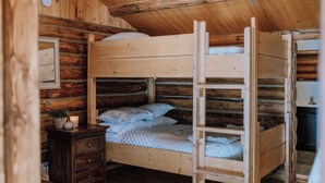 Ein Stockbett in einem Blockhauszimmer mit einem hölzernen Schminktisch und einem kleinen Tisch mit einer Kerze.