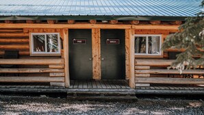 Eine Blockhütte mit zwei Türen, die mit "Pine" und "Birch" beschriftet sind, Holzbanken und einem Metalldach.