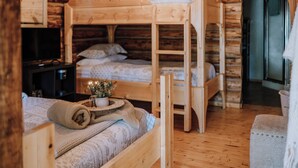 Ein gemütliches Blockhauszimmer mit Etagenbetten, einem kleinen Schreibtisch und einem Fernseher.