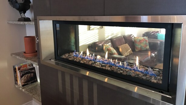 Ein moderner Kamin mit Glasscheibe, umgeben von einem Steinsockel und einem Metallrahmen.