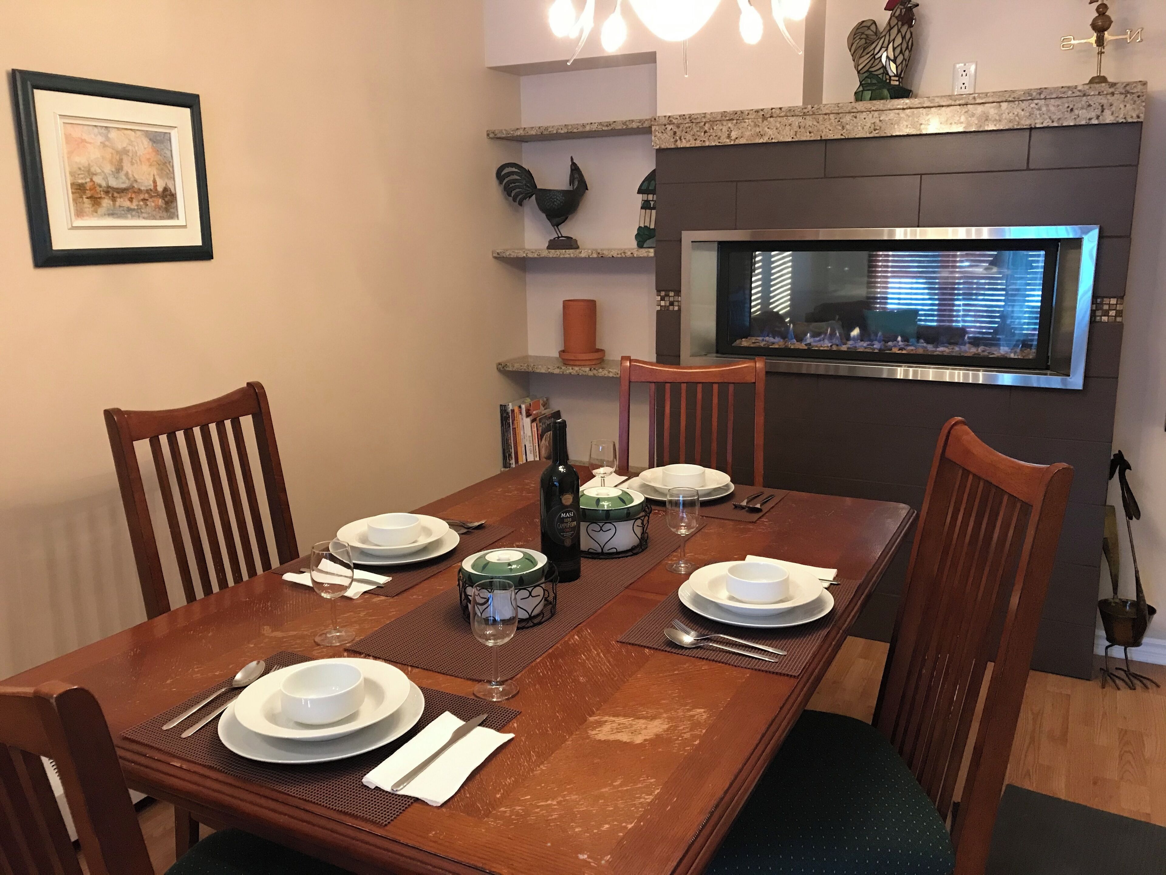 Un comedor con una mesa de madera dispuesta para dos personas, un televisor montado encima y una chimenea abajo.