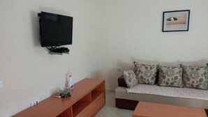 A living room with a TV mounted on the wall, a wooden entertainment unit, a sofa with patterned cushions, and a framed picture on the wall. - Apartments Lux Lukić Utjeha - One bedroom apartment (Utjeha)