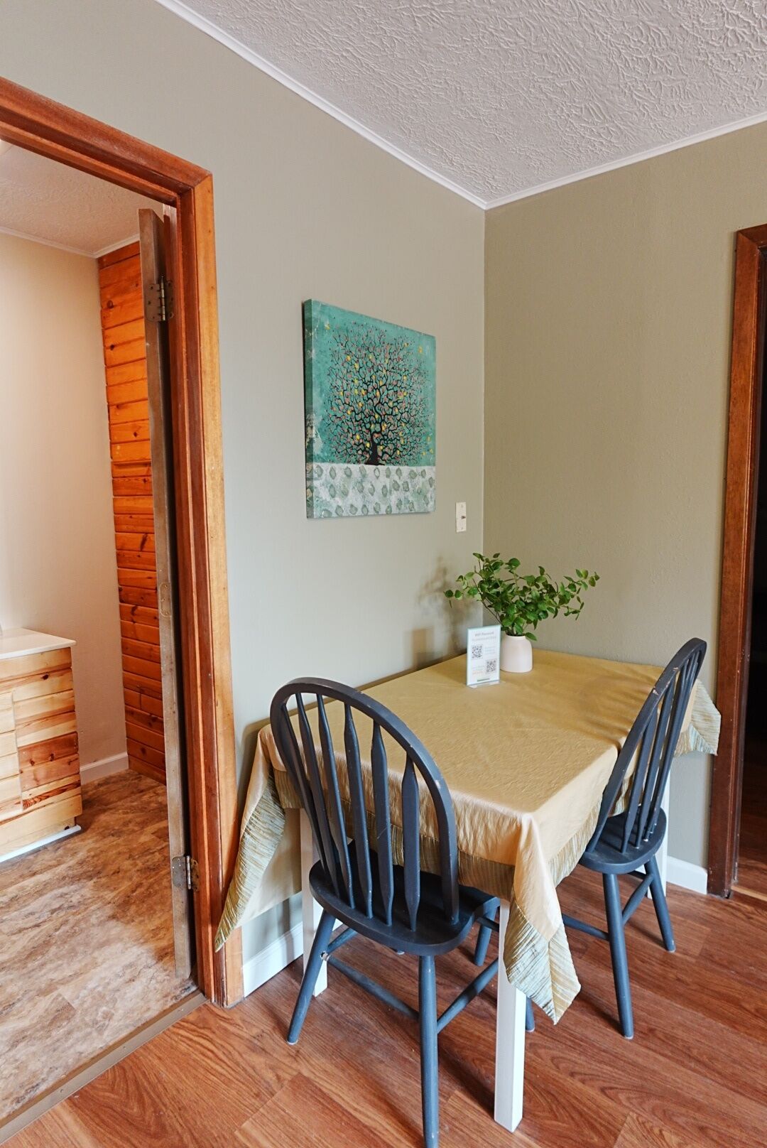 Un comedor con una mesa, sillas, una planta y un cuadro en la pared.