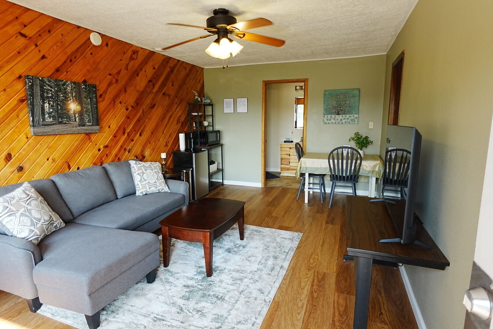 A living room with a gray sectional sofa, a wooden coffee table, and a dining area with a table and chairs.