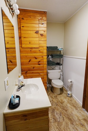 A bathroom with a wooden panel wall, a white sink, a toilet, and a towel rack. - Homestead Motel & RV (Sloan)