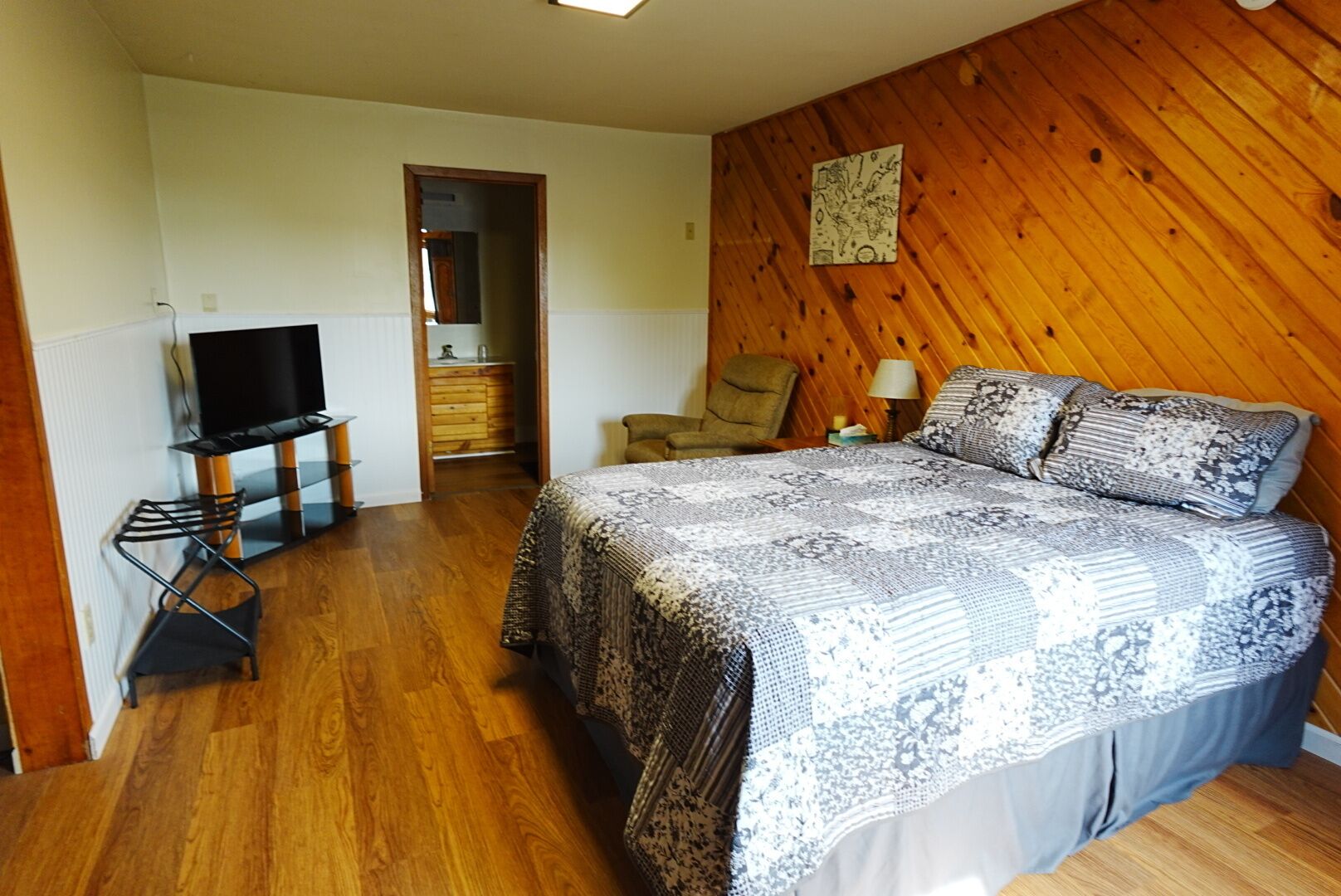 A bedroom with a bed, a television, a chair, and a wooden wall.