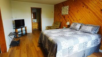 A bedroom with a bed, a television, a chair, and a wooden wall.