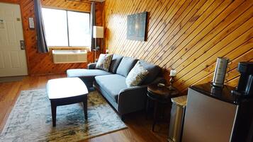 A room with a sofa, a small table, a lamp, a coffee maker, and a wall-mounted TV.