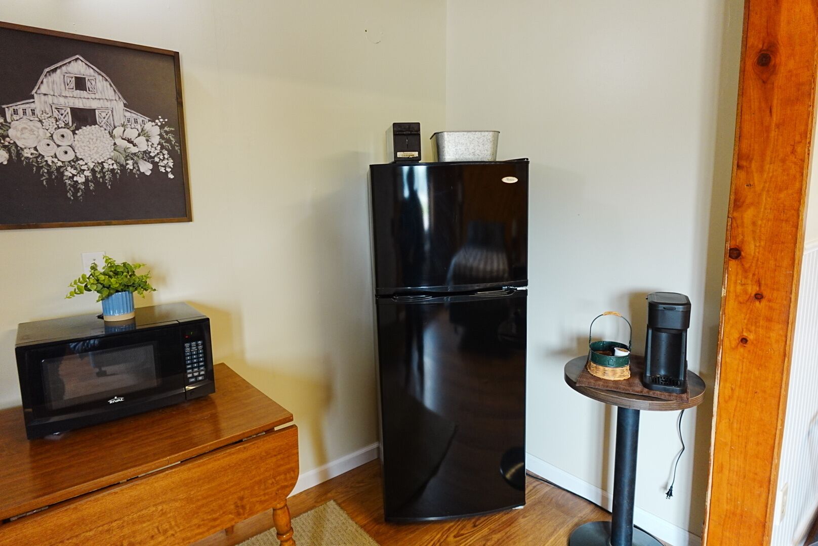 A compact kitchen with a refrigerator, microwave, and a small table with a plant.