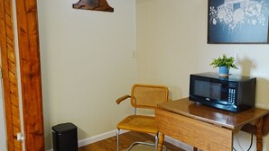 A room with a wooden desk, a chair, a trash bin, a microwave, and a framed picture on the wall. - Homestead Motel & RV (Sloan)