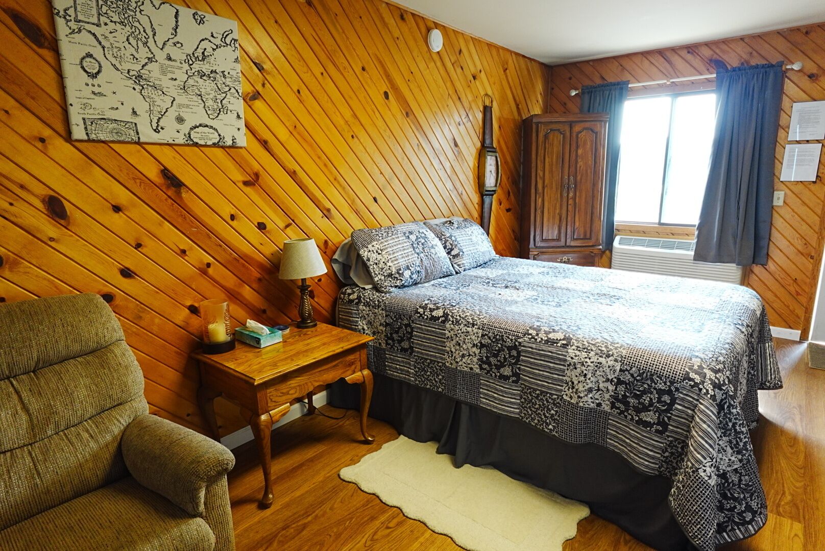 A room with a bed, a desk, a chair, a map on the wall, and a window with curtains.