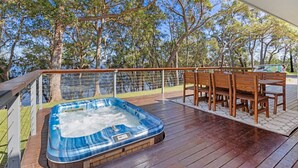 Une terrasse en bois avec un jacuzzi, des chaises en bois et une table.