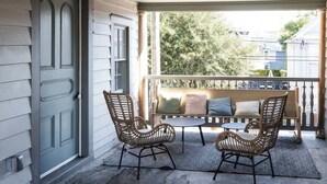 A covered porch with wicker chairs and a small table, a bench with cushions, and a view of trees and buildings. - The Grand Helène - Newly Renovated 11BD, 12BA - 2 Blocks from King St! (Charleston)