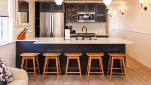 A modern kitchen with a central island, bar stools, stainless steel appliances, and a large window. - The Grand Helène - Newly Renovated 11BD, 12BA - 2 Blocks from King St! (Charleston)
