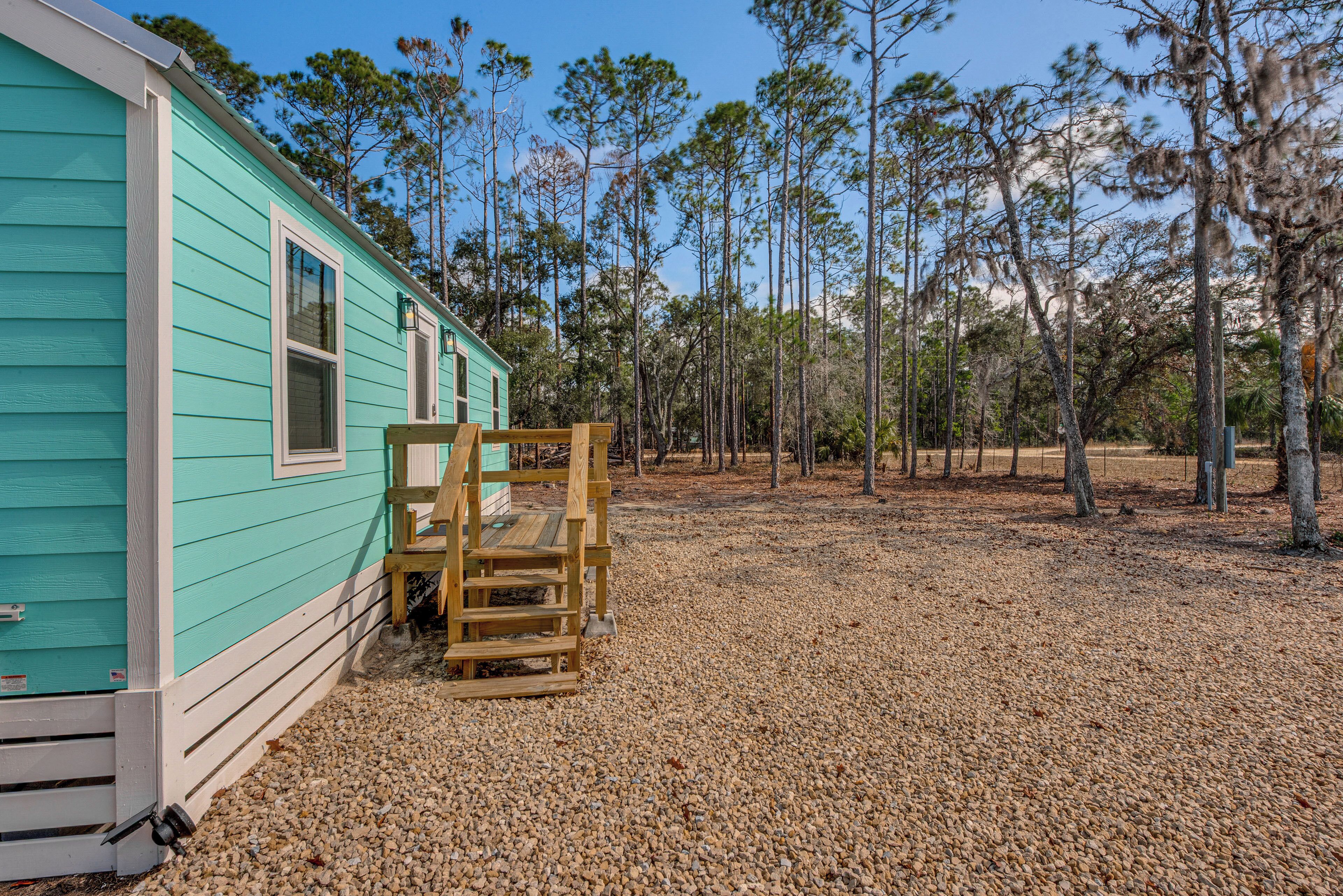 A turquoise cabin with a wooden deck and gravel ground.